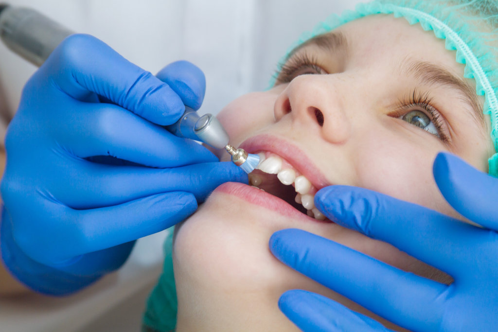 A woman dentist doctor brushes the teeth of a teenage child with a special medical brush. Inspection of the oral cavity of the girl. Modern technologies in dentistry.