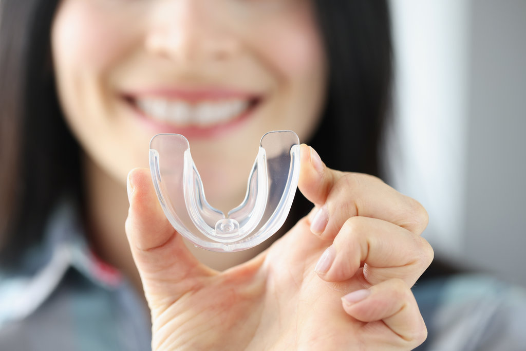 Smiling woman holds transparent plastic mouth guard in her hand. Correction of malocclusion and bruxism concept