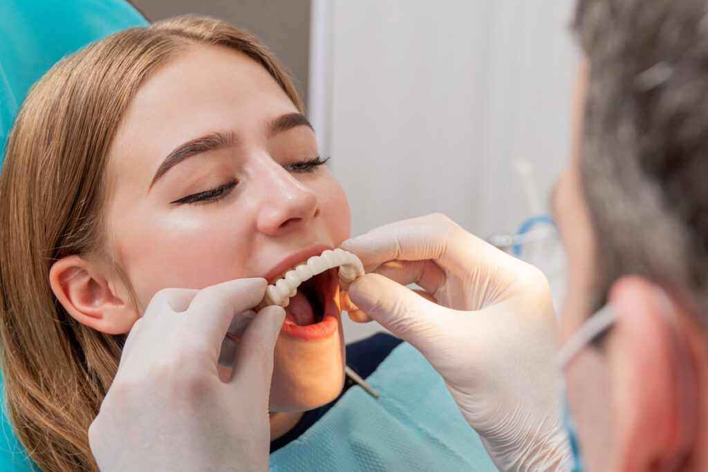 doctor tries on a denture on the upper teeth to a patient sitting in a chair