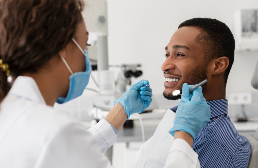 Young african guy smiling to his female dentist while having treatment at modern clinic