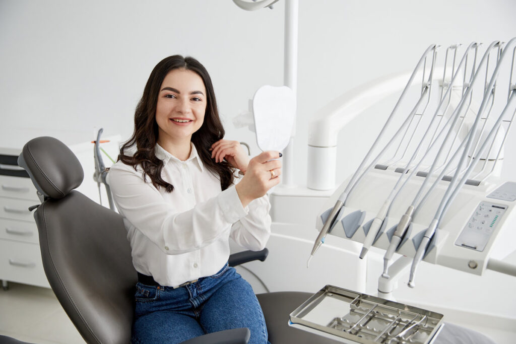 Happy woman patient checking teeth in mirror.